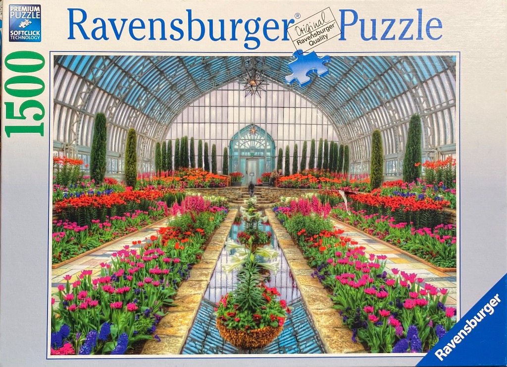 Interior view of a Victorian-style glass greenhouse with vibrant flower beds and a central reflection pool.
