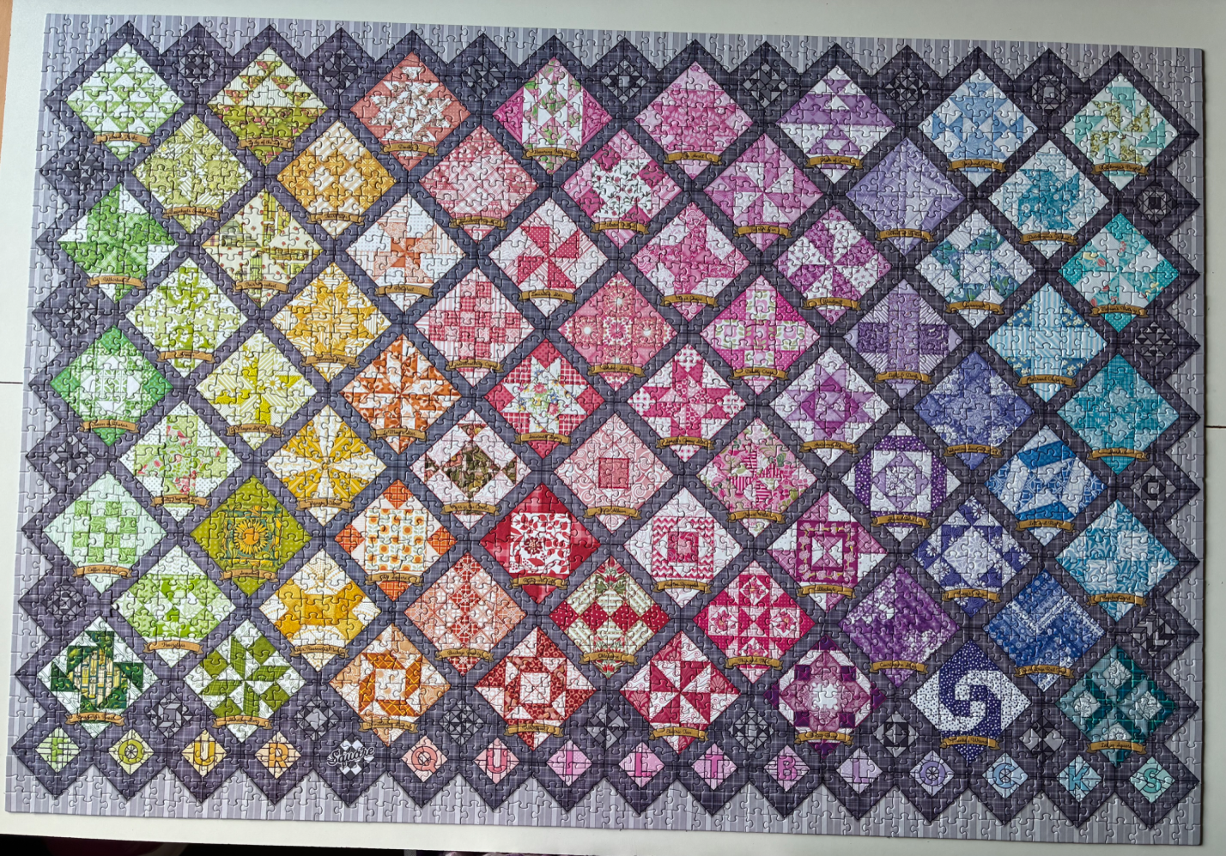 A quilt-themed graphic featuring an array of colorful, patterned diamond-shaped blocks in a spectrum gradient.