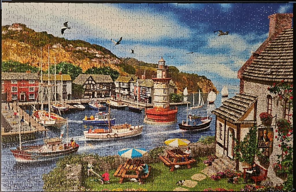 A bustling harbor village scene with boats, a lighthouse, and a foreground garden with people.