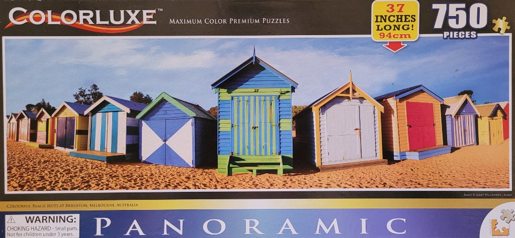 A row of colorful wooden beach huts on a sandy Australian beach under a bright blue sky.