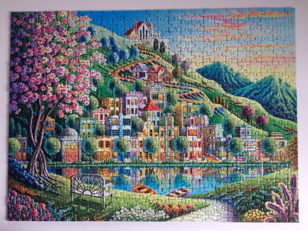 A whimsical painting of a colorful hillside village overlooking a reflective pond at sunset.