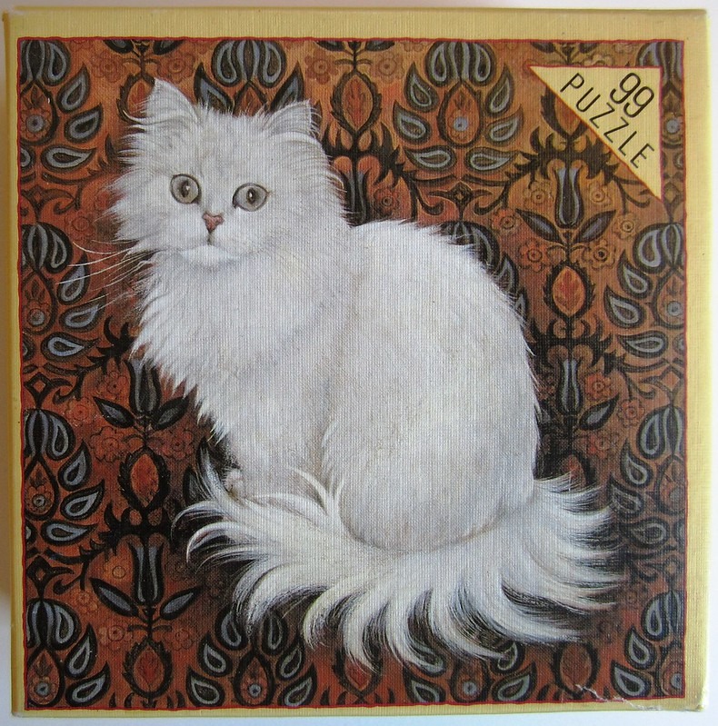 A fluffy white long-haired cat sitting against a dark, intricate floral and paisley-patterned wallpaper background.