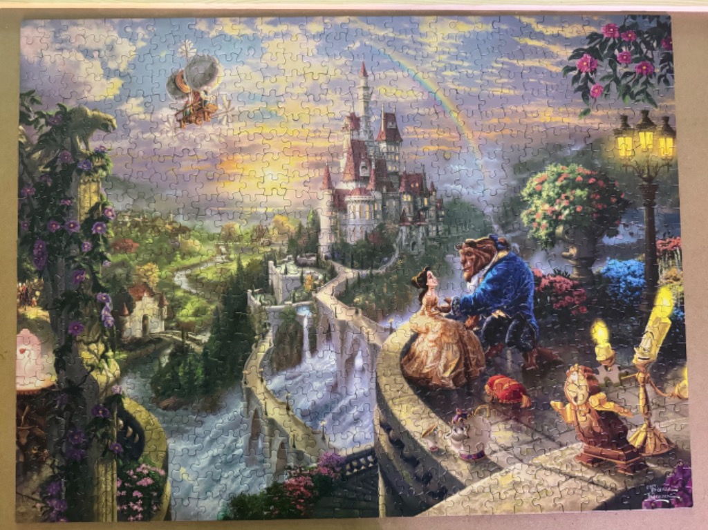 Belle and the Beast standing on a balcony overlooking a fairytale castle at sunset