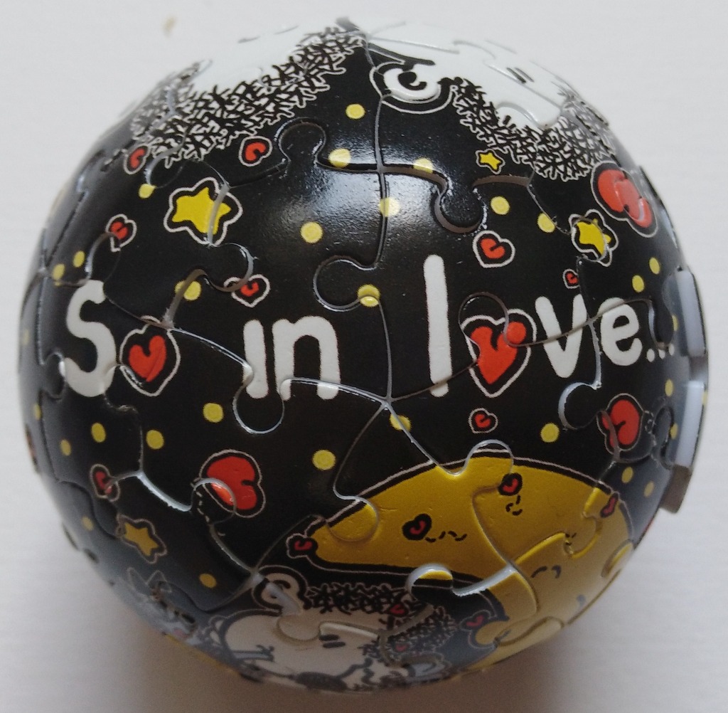 A spherical object decorated with a black background, white text reading 'So in love...', stars, hearts, and a yellow crescen