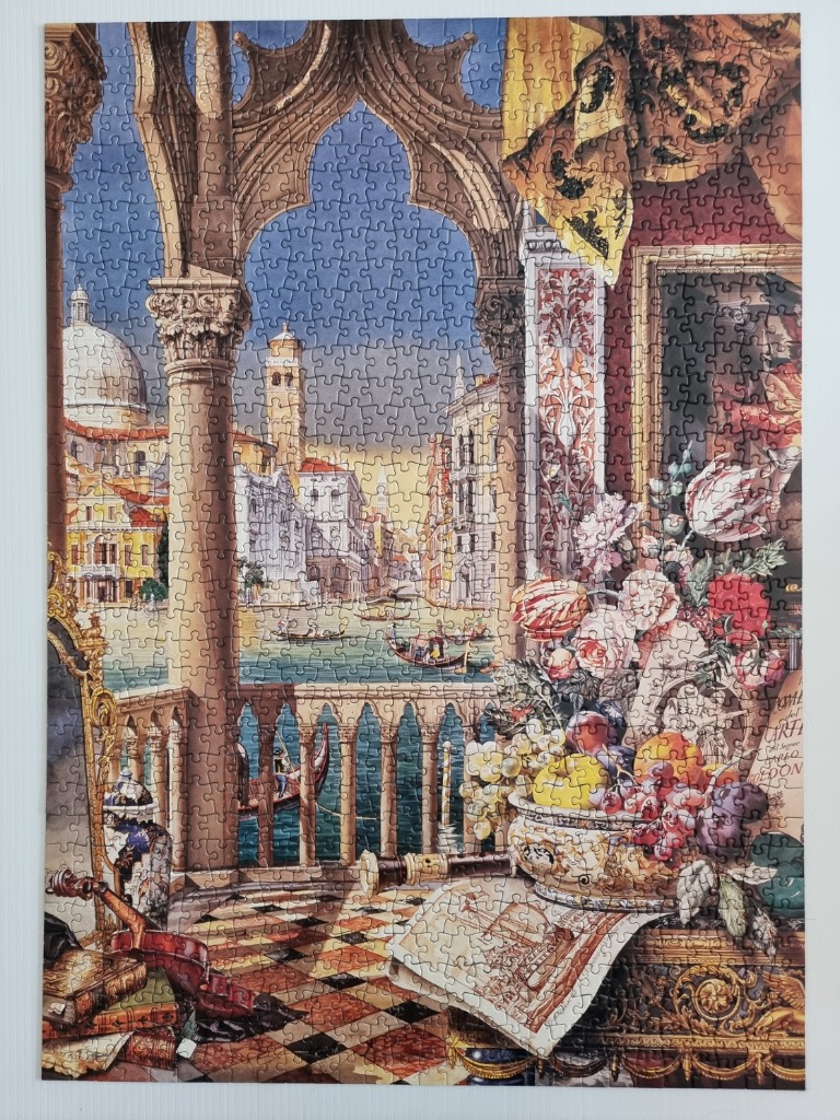 An ornate balcony overlooking a Venetian canal with a still life of fruit and flowers in the foreground.