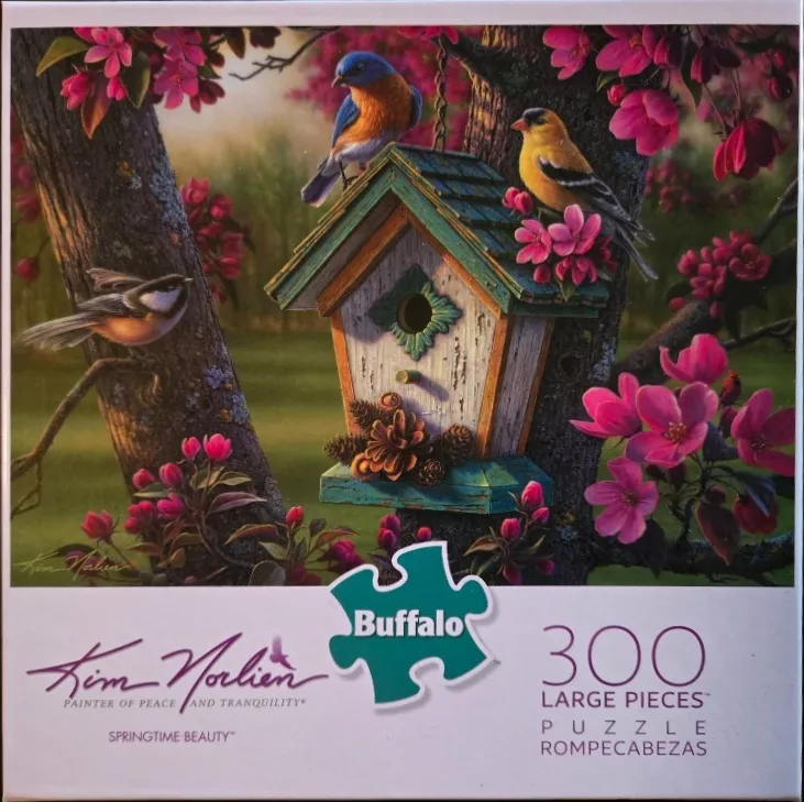 A birdhouse nestled in a tree with pink blossoms and three songbirds.