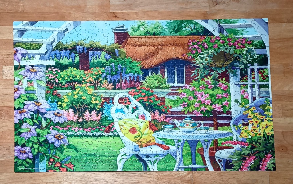 A peaceful garden scene with a white wrought-iron table and chair in front of a thatched-roof cottage.