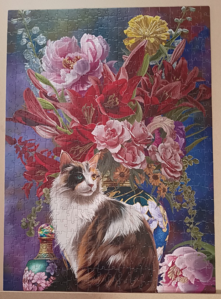 A fluffy calico cat sitting in front of a vibrant bouquet of flowers in a decorative blue vase.
