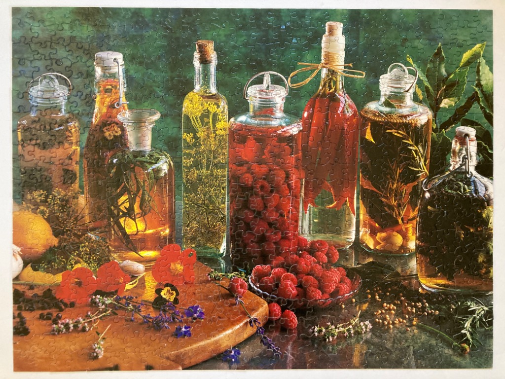 Collection of glass bottles filled with infused oils, vinegars, berries, and herbs on a wooden surface.