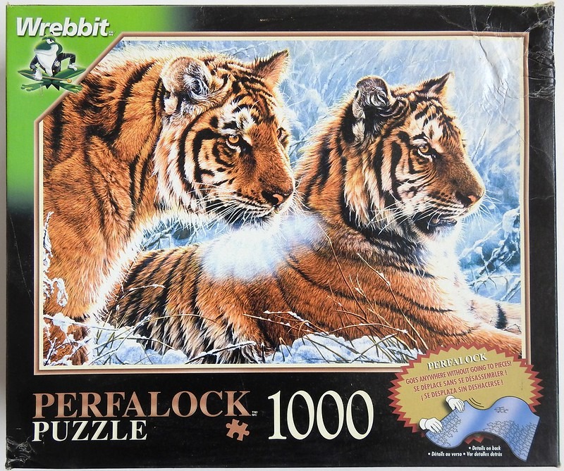 Two tigers resting in a snowy, winter forest landscape.