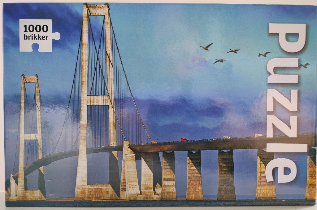 The Great Belt Bridge spanning across water under a dramatic blue and purple sky with birds flying overhead.