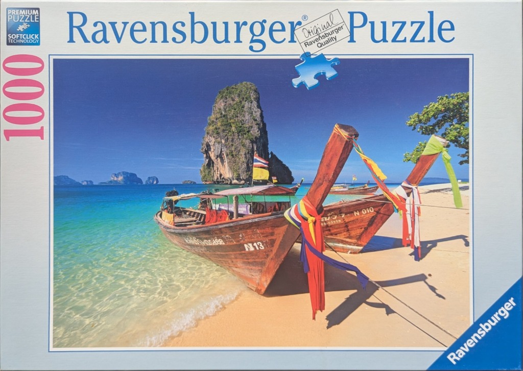 Two traditional longtail boats docked on a sunny tropical beach in Thailand with limestone cliffs in the background.