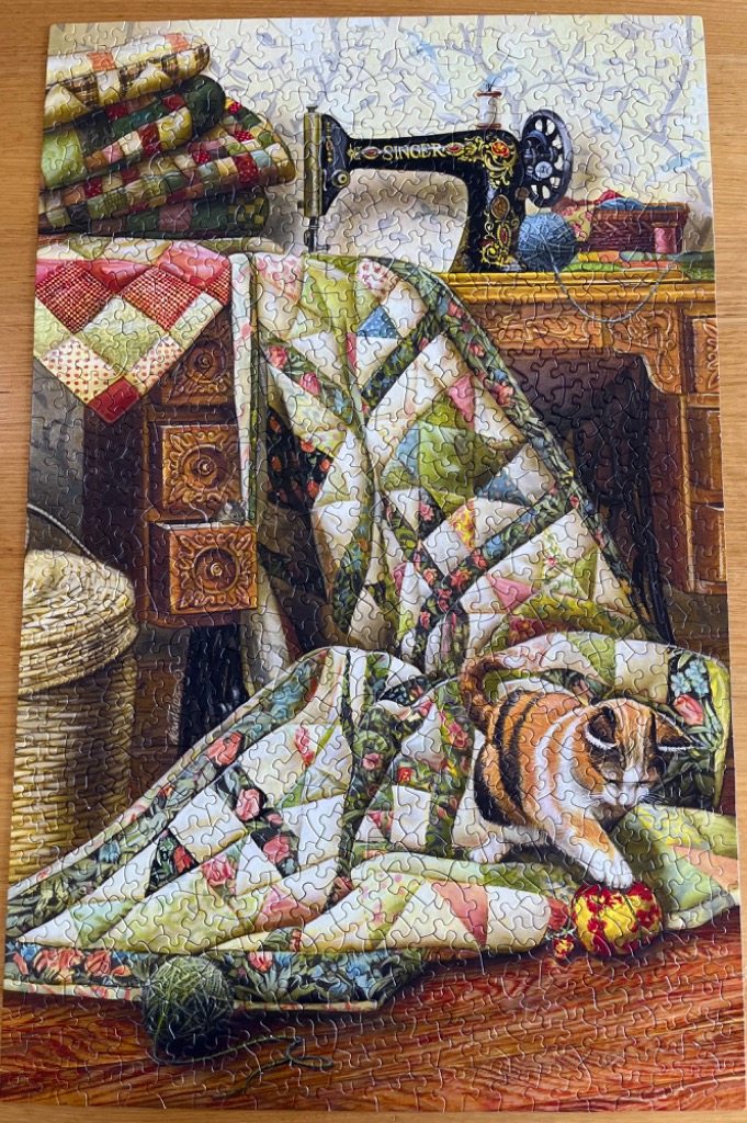 A vintage sewing machine, a stack of patchwork quilts, and a calico cat on a wooden floor.