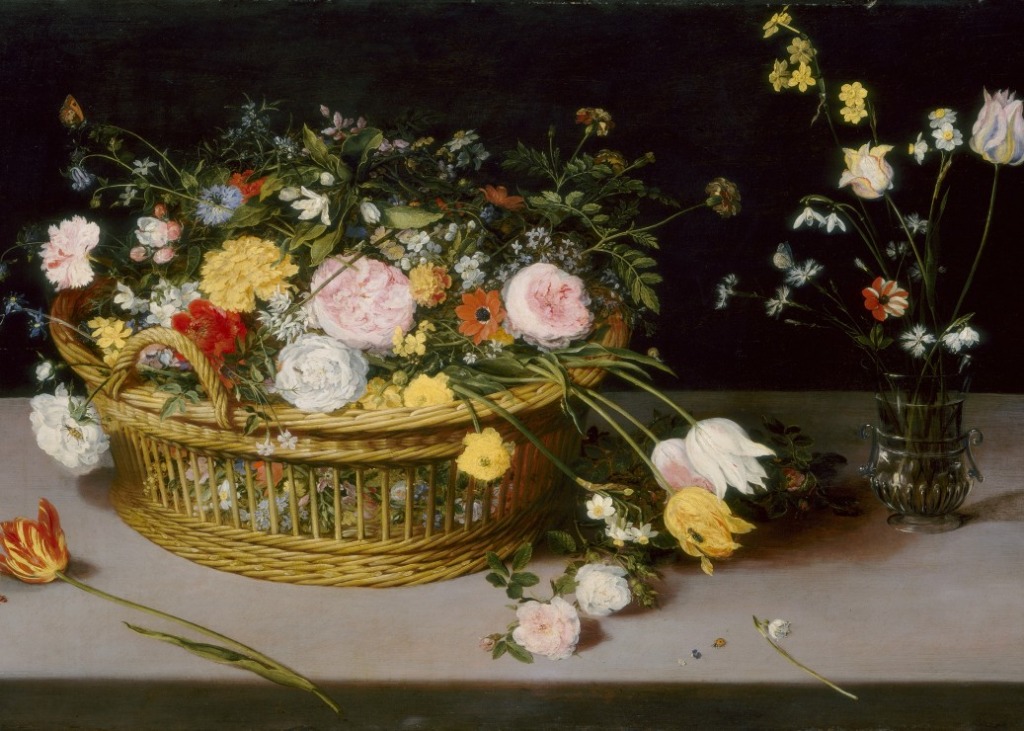 A wicker basket overflowing with flowers next to a small glass vase on a stone ledge against a dark background.
