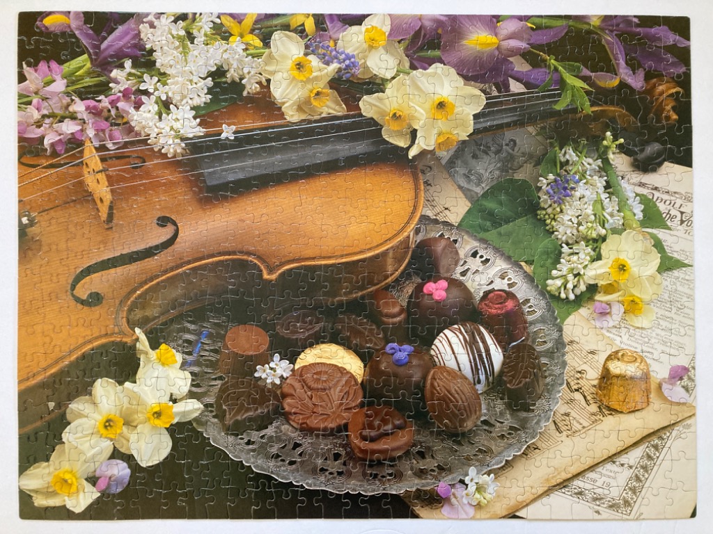 Still life of a wooden violin, spring flowers, and a silver platter of chocolates on sheet music.