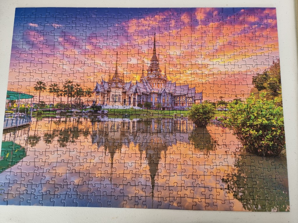 A Thai-style temple reflecting in a calm pond during a vibrant purple and orange sunset.