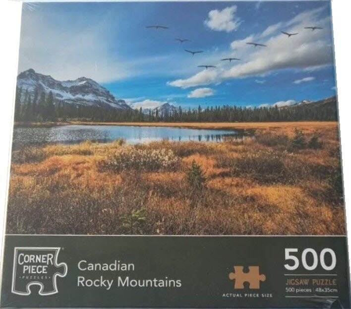 Landscape of the Canadian Rocky Mountains featuring a lake, golden marshland, and a flock of birds against a blue sky.