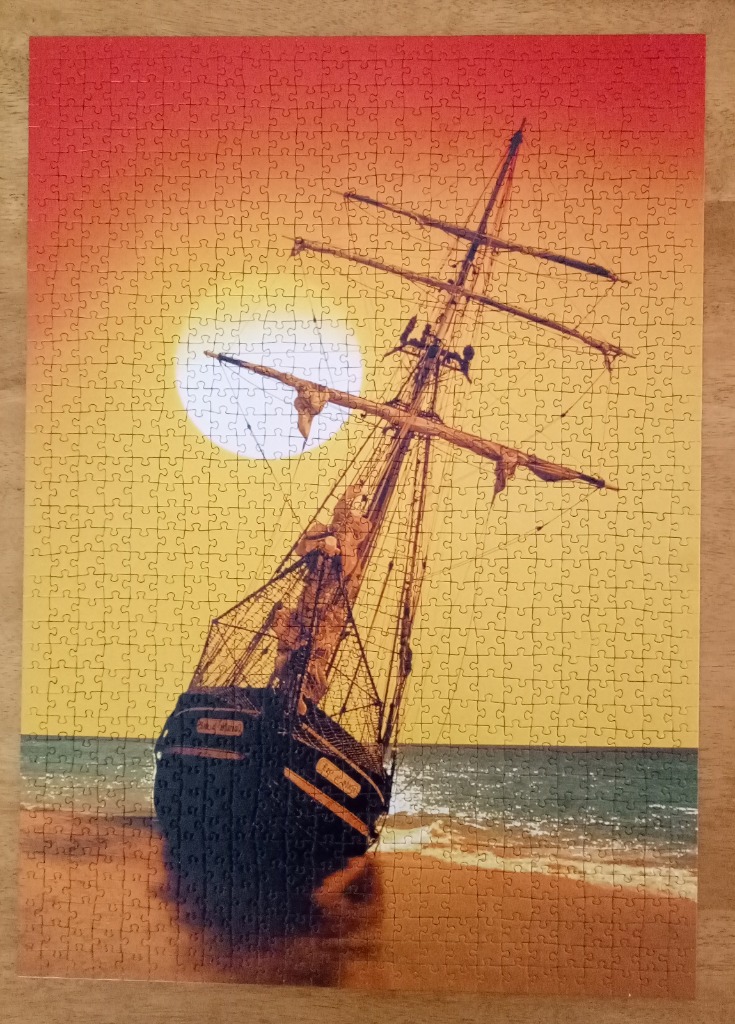 A tall-masted ship beached on a sandy shore at sunset.