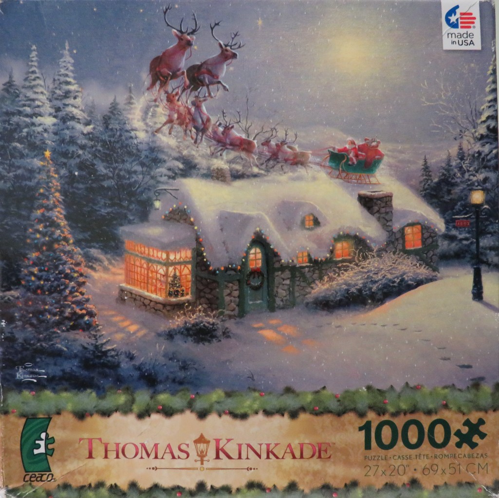 Santa Claus and his reindeer flying over a snow-covered cottage at night.