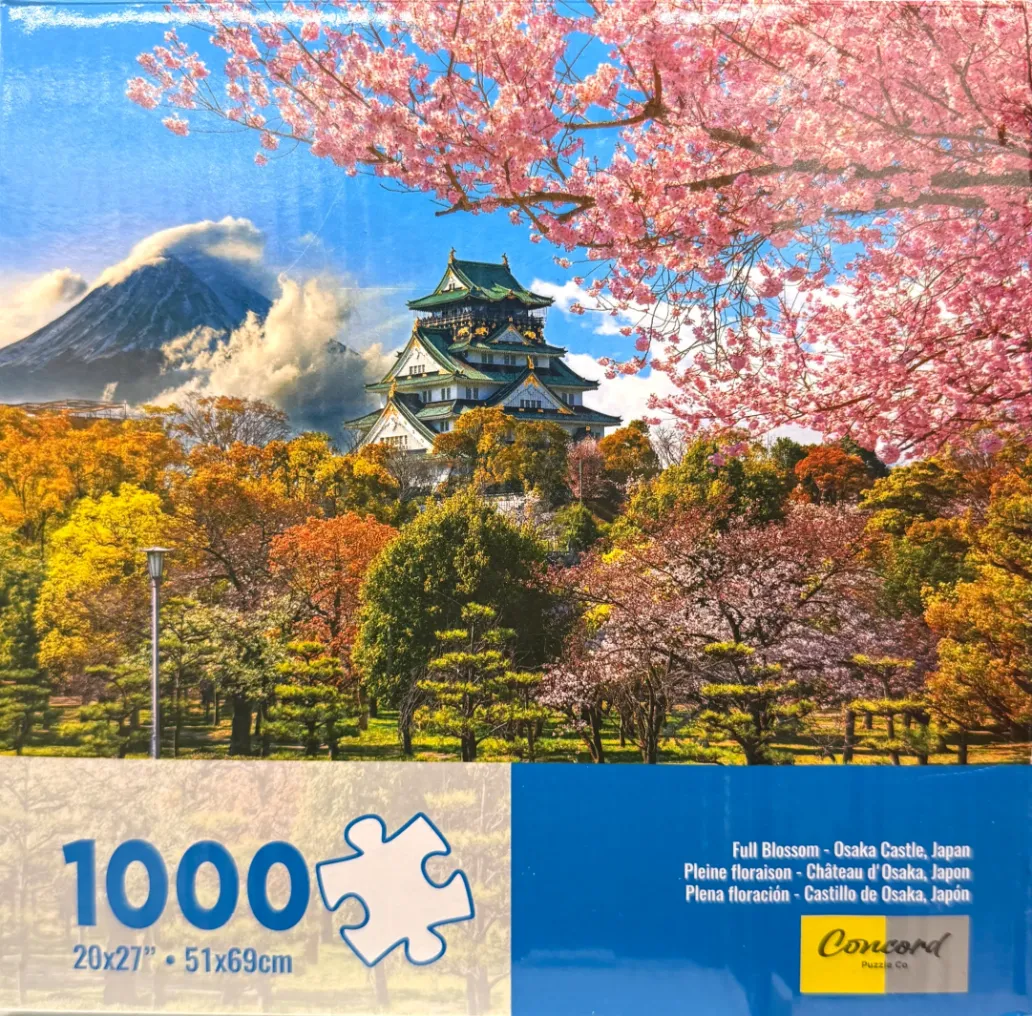 Osaka Castle surrounded by cherry blossoms and autumn trees with a distant mountain peak under a blue sky.