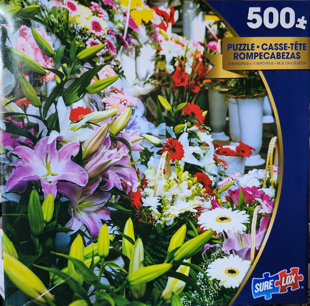 A close-up photograph of a floral shop display featuring purple lilies, white daisies, and red gerbera flowers.