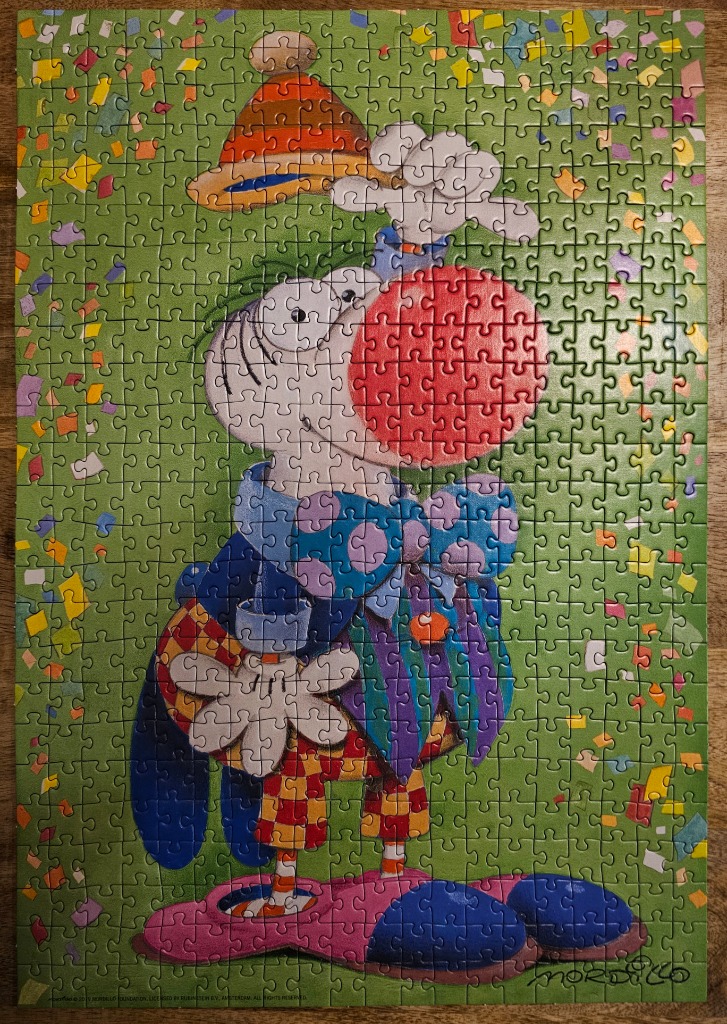 A cartoon illustration of a whimsical, round-nosed clown character standing amidst falling confetti against a green backgroun