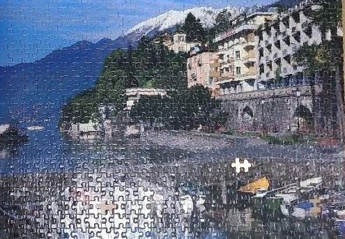 A scenic view of a European lakeside town with snow-capped mountains in the background.