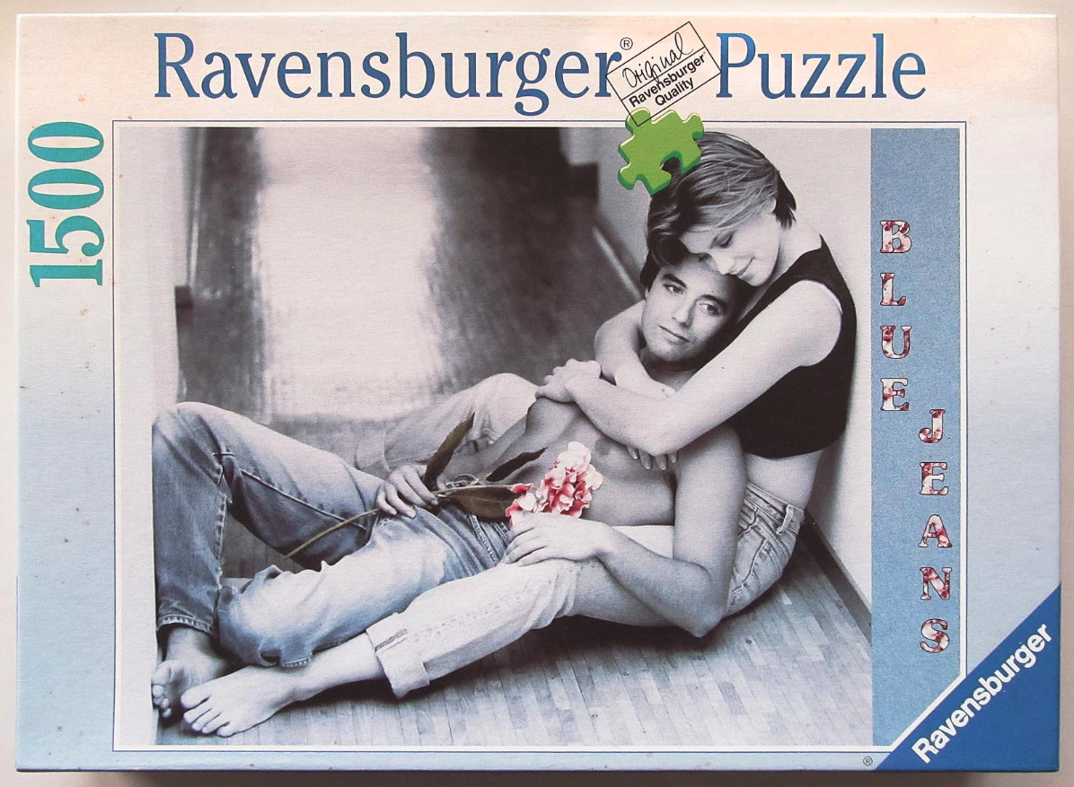 A black and white photograph of a young couple embracing on a floor, holding a pink flower.