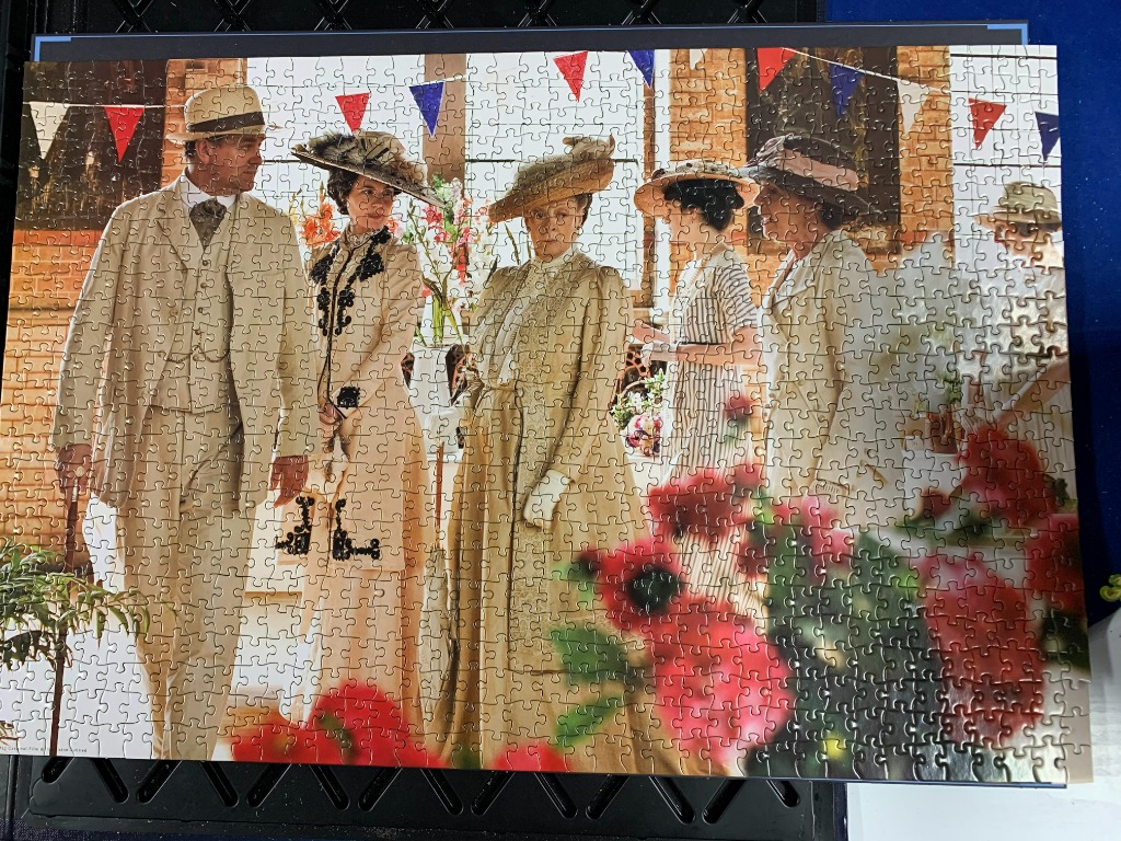 A group of Edwardian-era figures in formal garden party attire, decorated with red and blue bunting.
