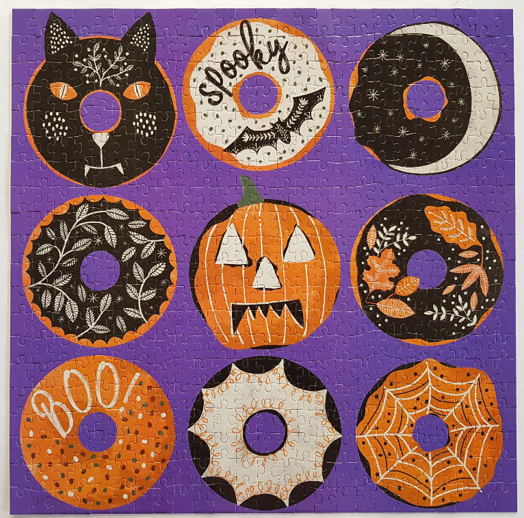 A Halloween-themed grid of nine circular, decorated doughnuts on a purple background.