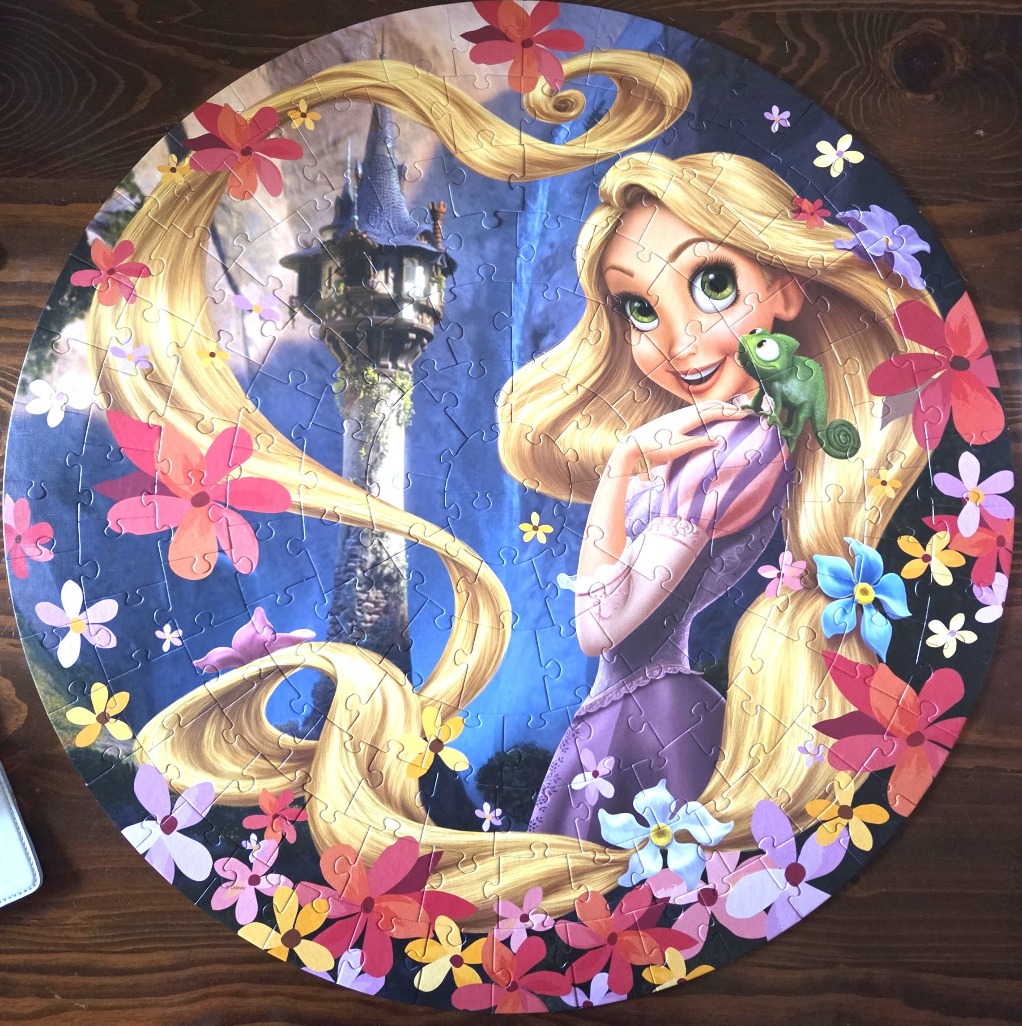 Rapunzel and her chameleon friend Pascal in front of her tower, surrounded by flowers.