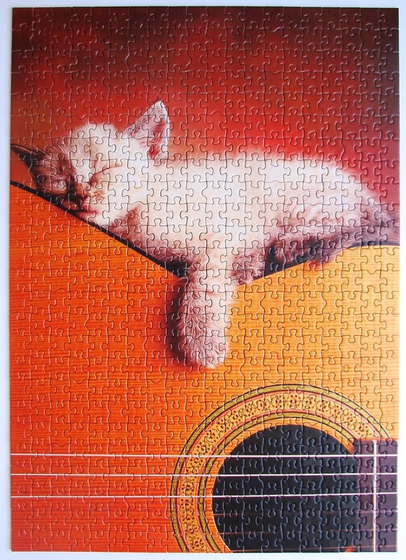 A small, fluffy kitten sleeping peacefully draped across the body of an acoustic guitar.