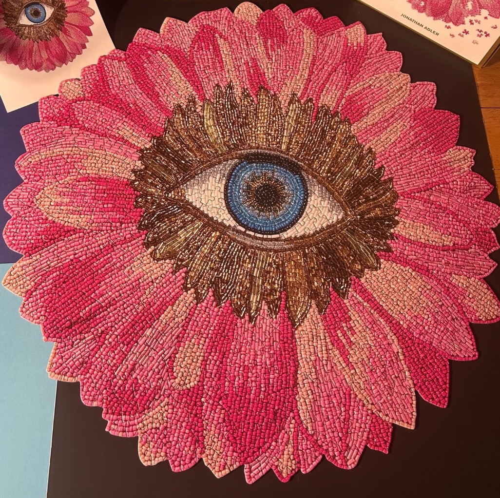 A circular image featuring a pink flower with a realistic human eye in the center, rendered in a bead-like texture.