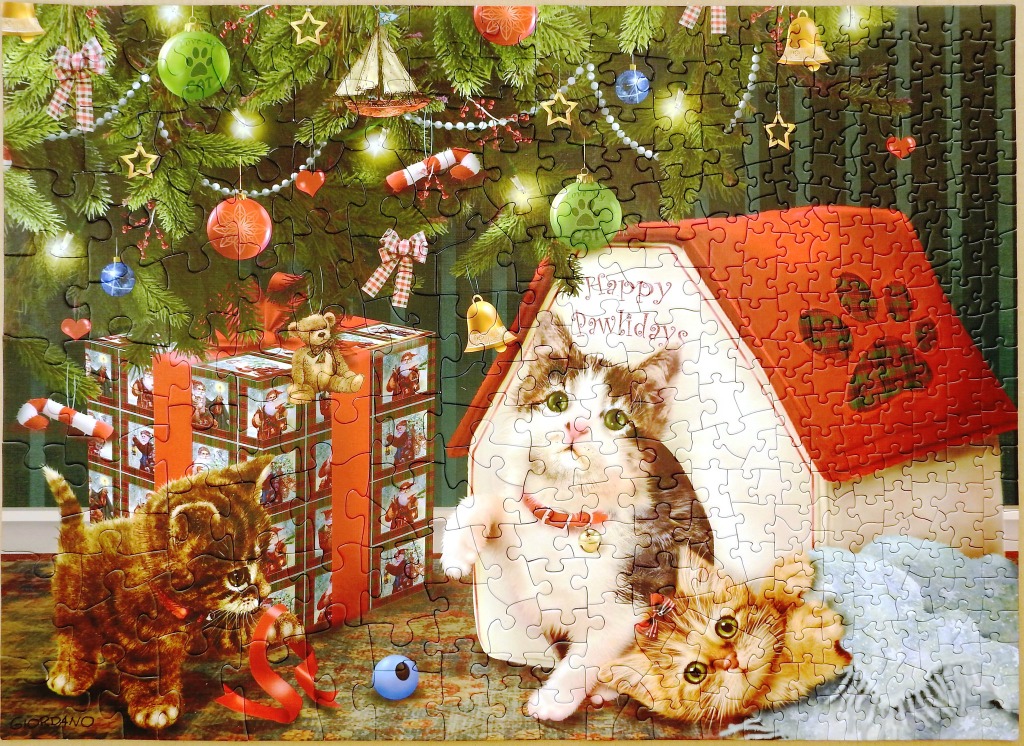 Three kittens around a Christmas tree, a gift box, and a dog house with the text Happy Pawlidays.