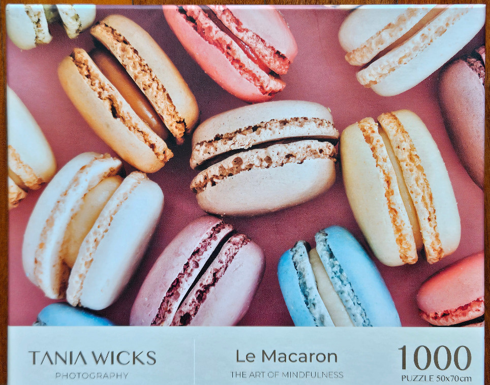 A close-up photograph of assorted colorful macarons arranged on a dusty rose pink background.