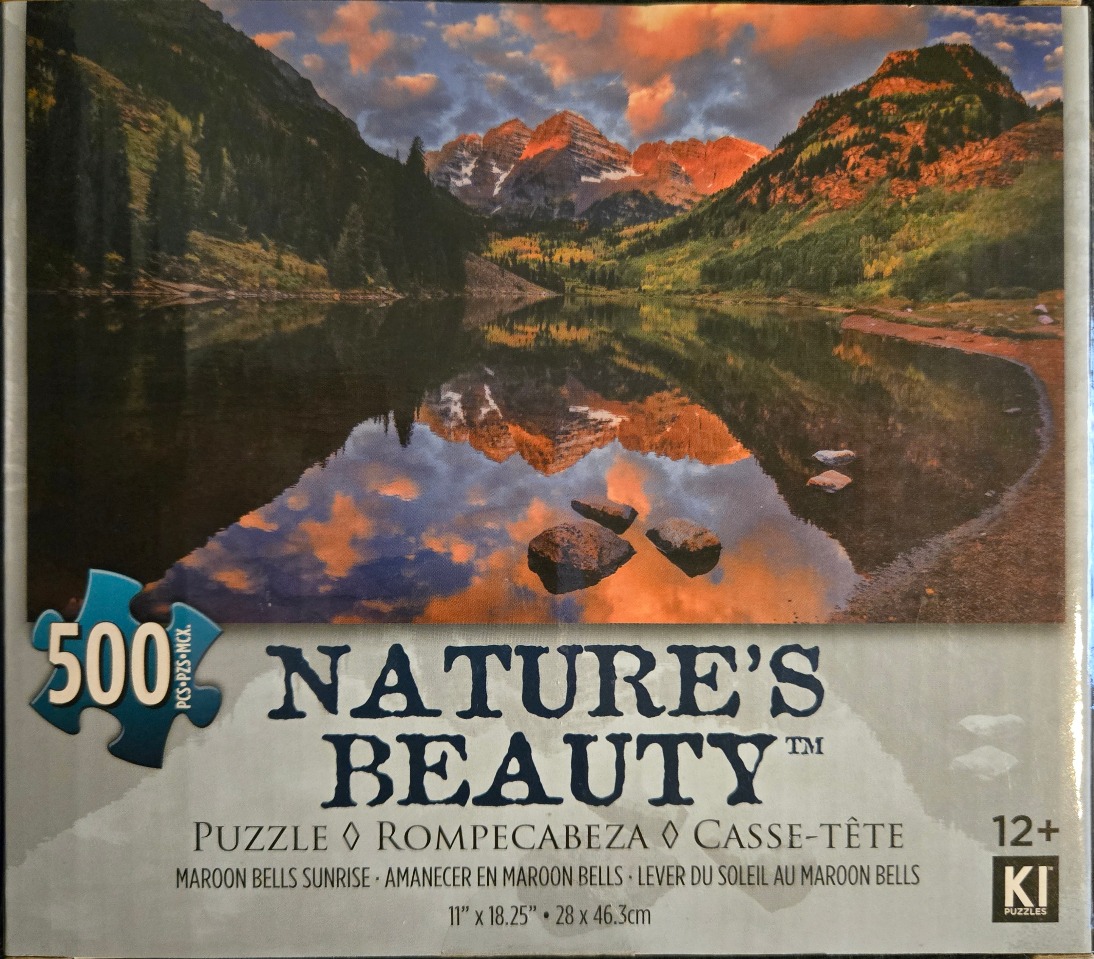 A photograph of the Maroon Bells peaks in Colorado at sunrise, reflected in a calm alpine lake.