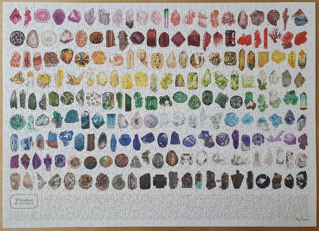 A collection of various crystals and minerals arranged in a rainbow-spectrum grid against a white background.