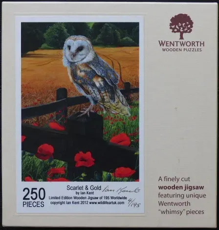A barn owl perched on a black fence in a field of poppies with golden wheat in the background.