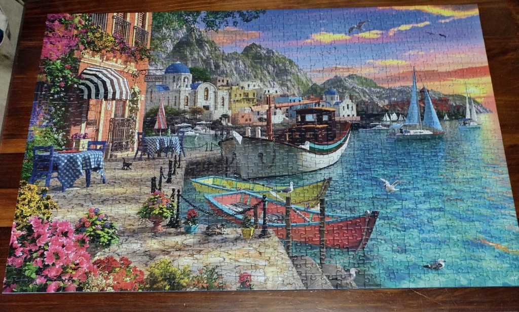 A scenic Greek coastal village at sunset with a taverna terrace and docked boats.