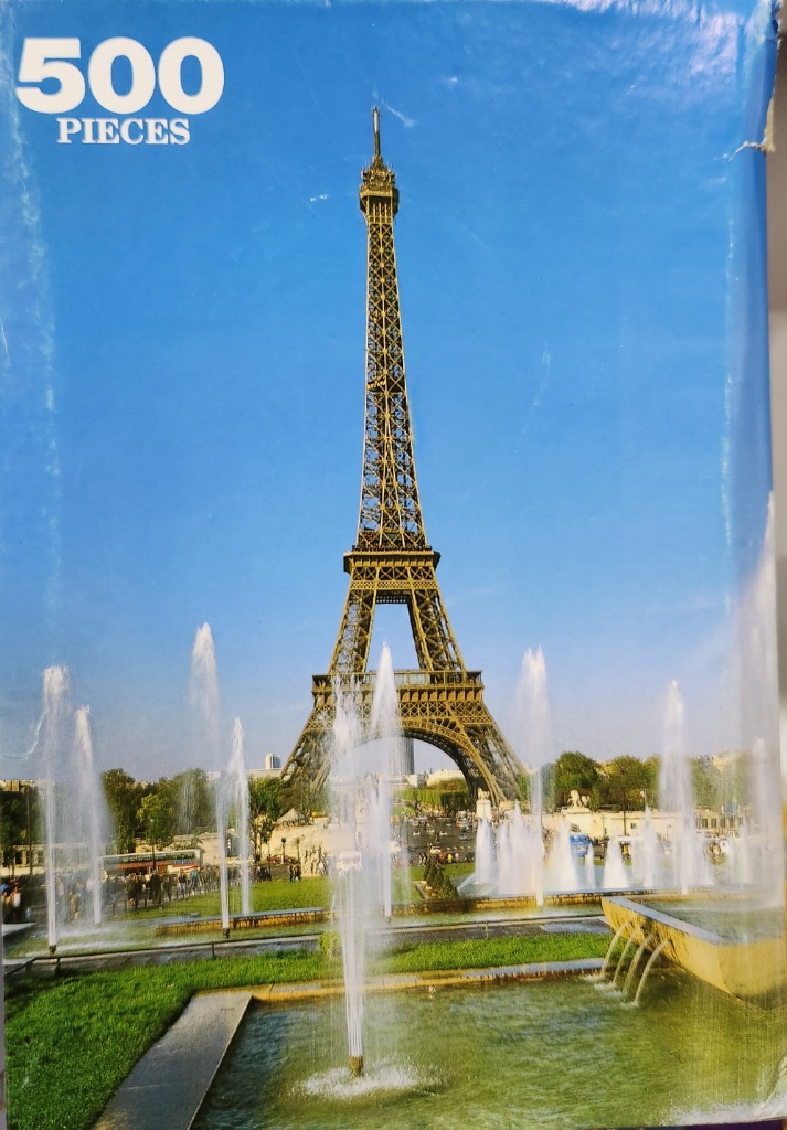 The Eiffel Tower rising behind a park fountain under a bright blue sky.