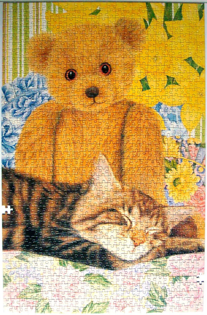A teddy bear sitting behind a sleeping tabby cat, surrounded by colorful garden flowers.