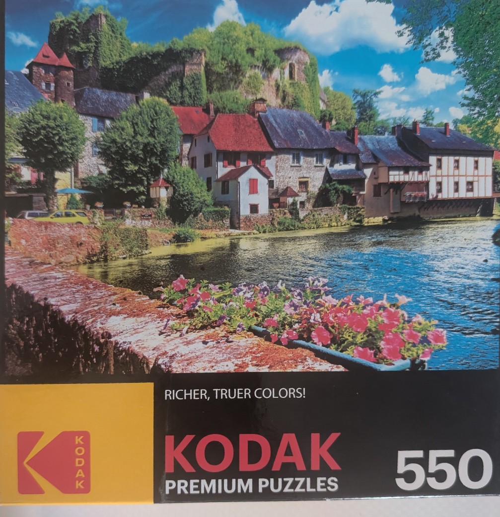 A picturesque European village with stone buildings, a river, and a fortress on a hill.