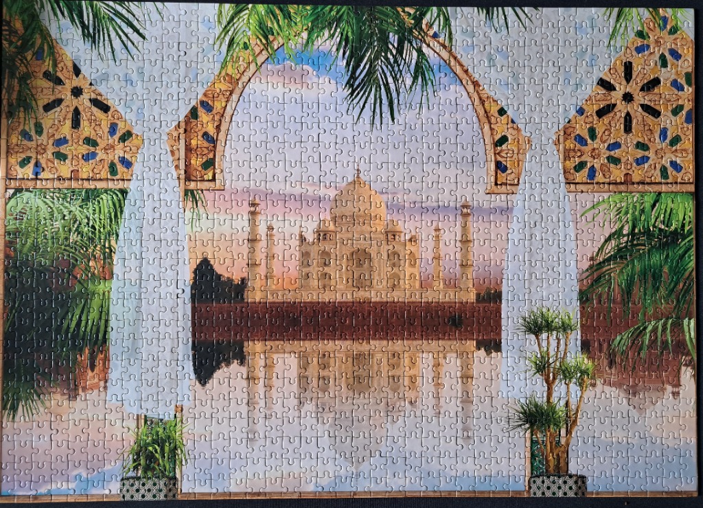 View of the Taj Mahal framed by ornate stone arches and lush tropical foliage at sunset.