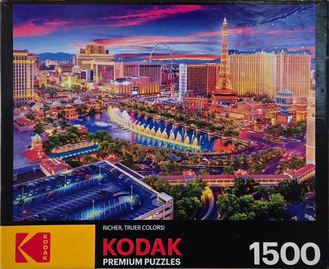 Nighttime panoramic view of the Las Vegas Strip with illuminated hotels, a fountain show, and a vibrant sunset sky.