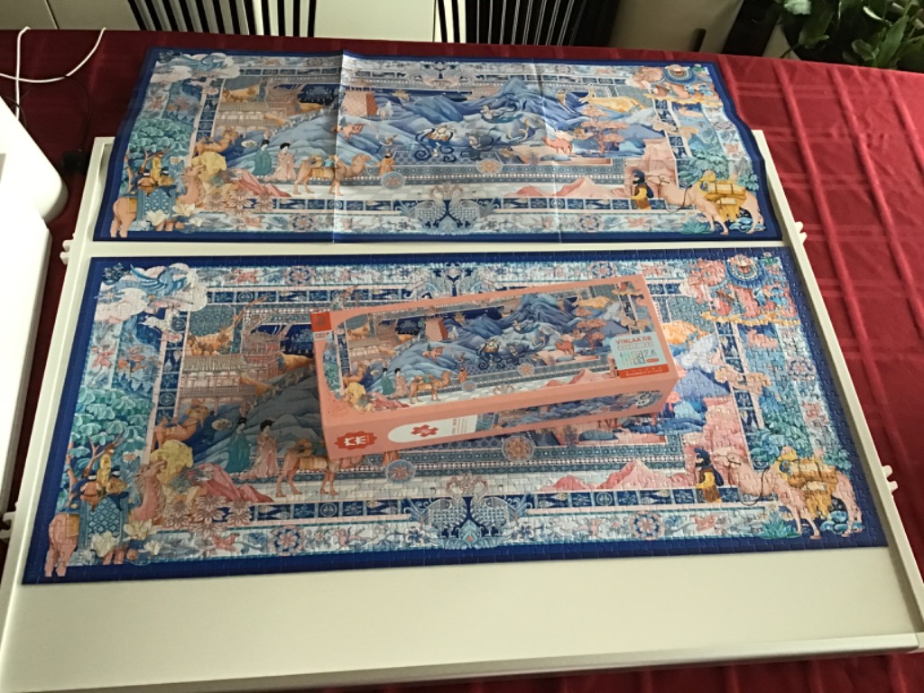 A panoramic scene of a Silk Road caravan set within a decorative border on a white table.