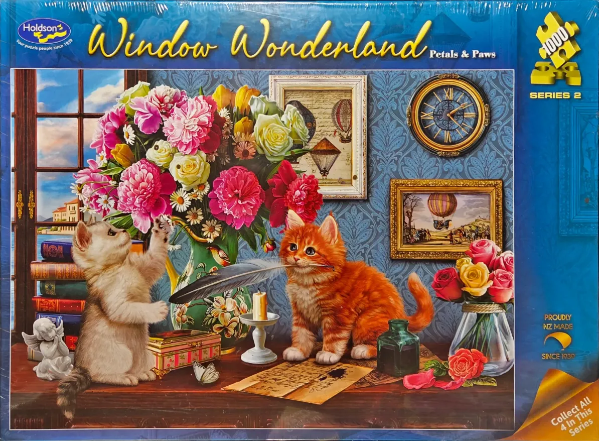 Two kittens playing on a desk with flowers and antique objects.