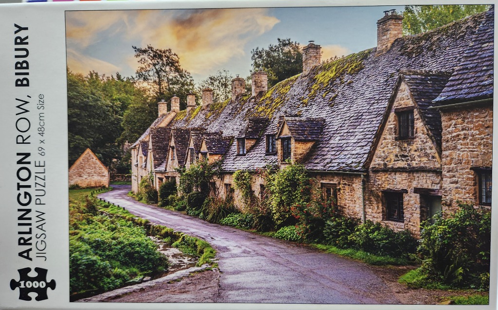 A picturesque row of historic Cotswold stone cottages in Bibury with a scenic lane and sunset sky.