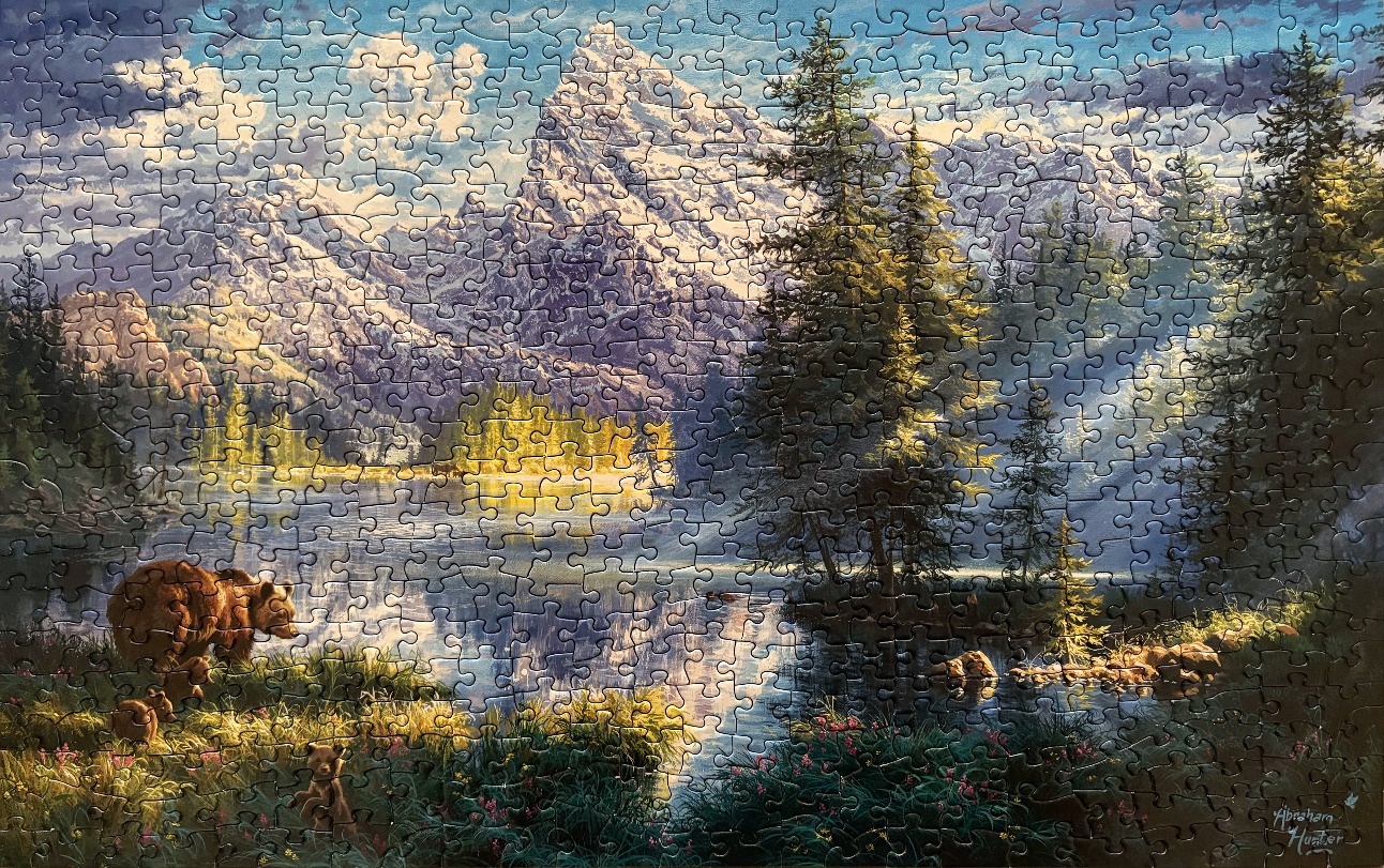 A mother grizzly bear and two cubs standing in a lush meadow by a mountain lake at sunrise.