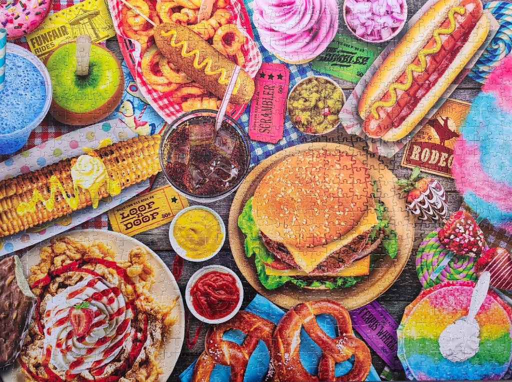 A top-down view of a colorful spread of classic fairground and carnival foods on a wooden table.