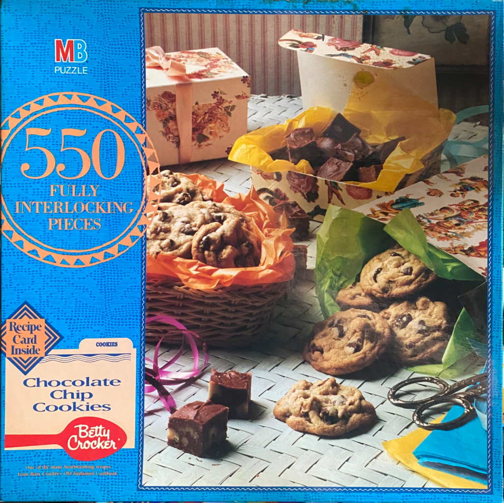 A still life photograph of chocolate chip cookies and fudge displayed for gifting in baskets and floral boxes.